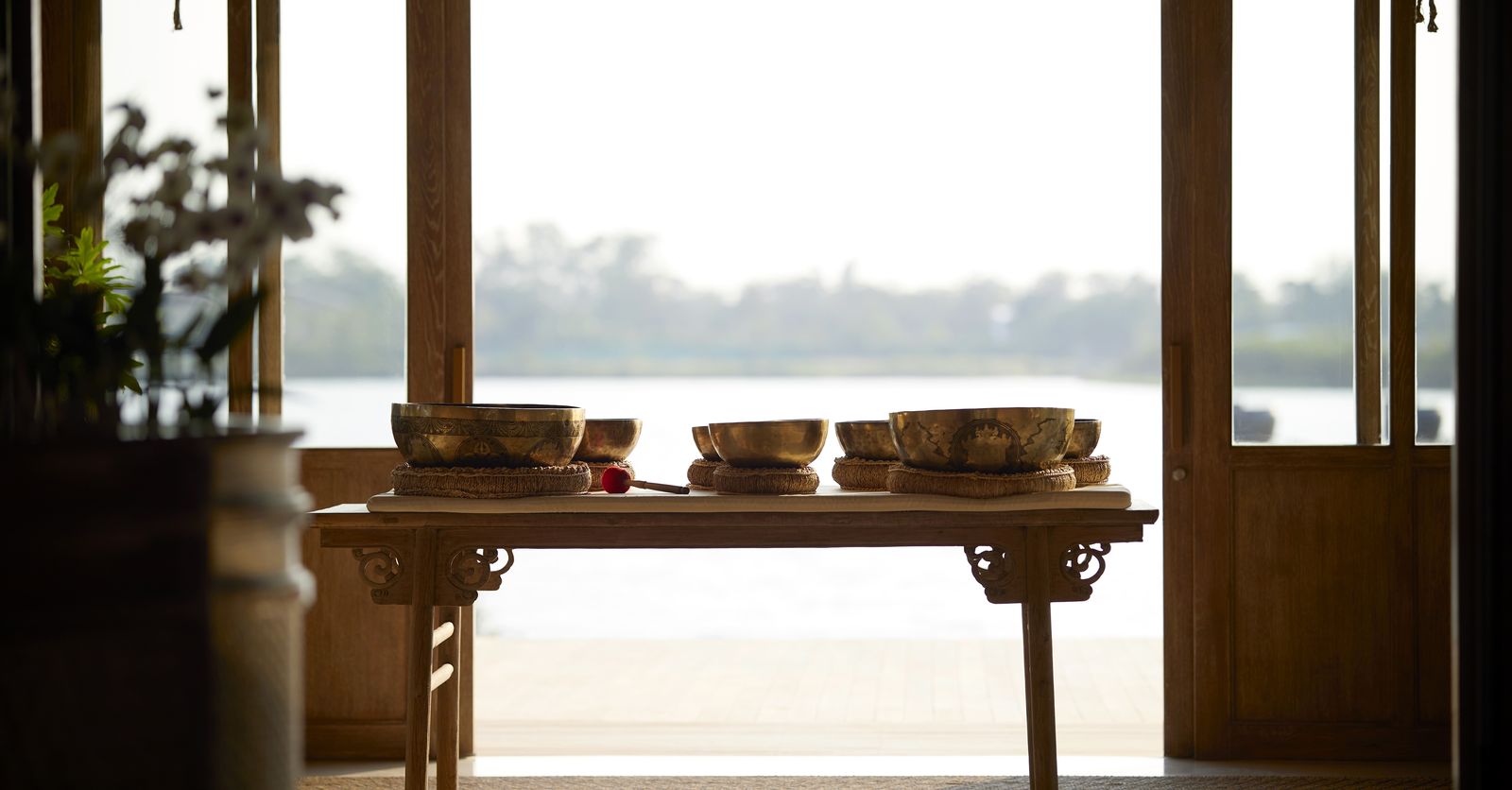 Tibetan singing bowls arranged on a wooden table in an open-air pavilion overlooking the river, RAKxa, Bang Krachao