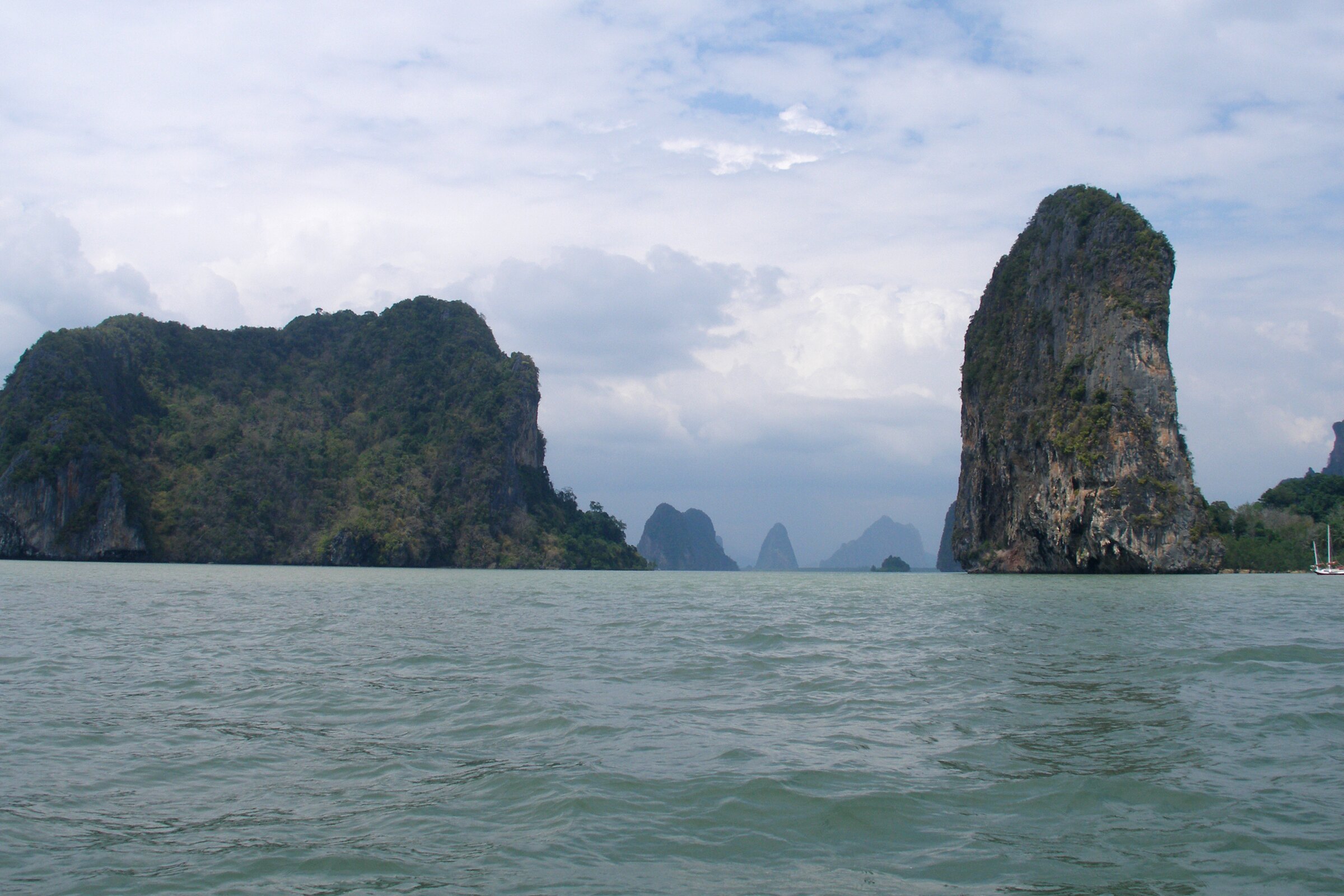 Limestone karsts rising sheer from the sea in Phang Nga Bay, more fading into haze behind