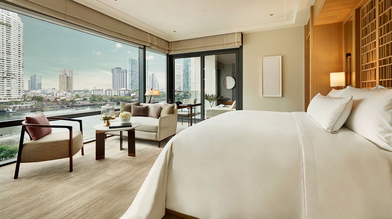 A Capella riverfront suite bedroom with floor-to-ceiling glass over the Chao Phraya and the Bangkok skyline