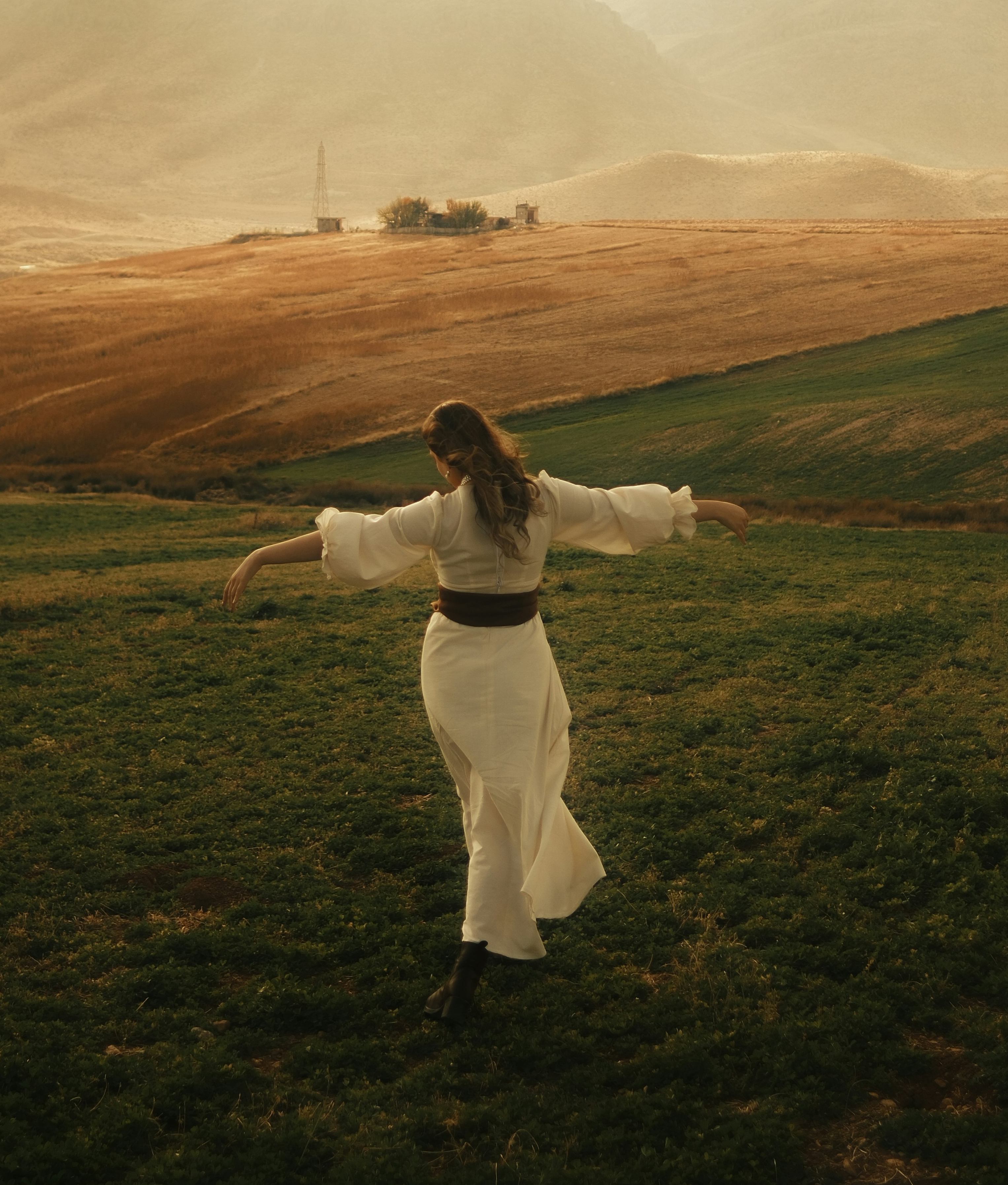 A woman in flowing white, arms outstretched, moving freely across an open hillside