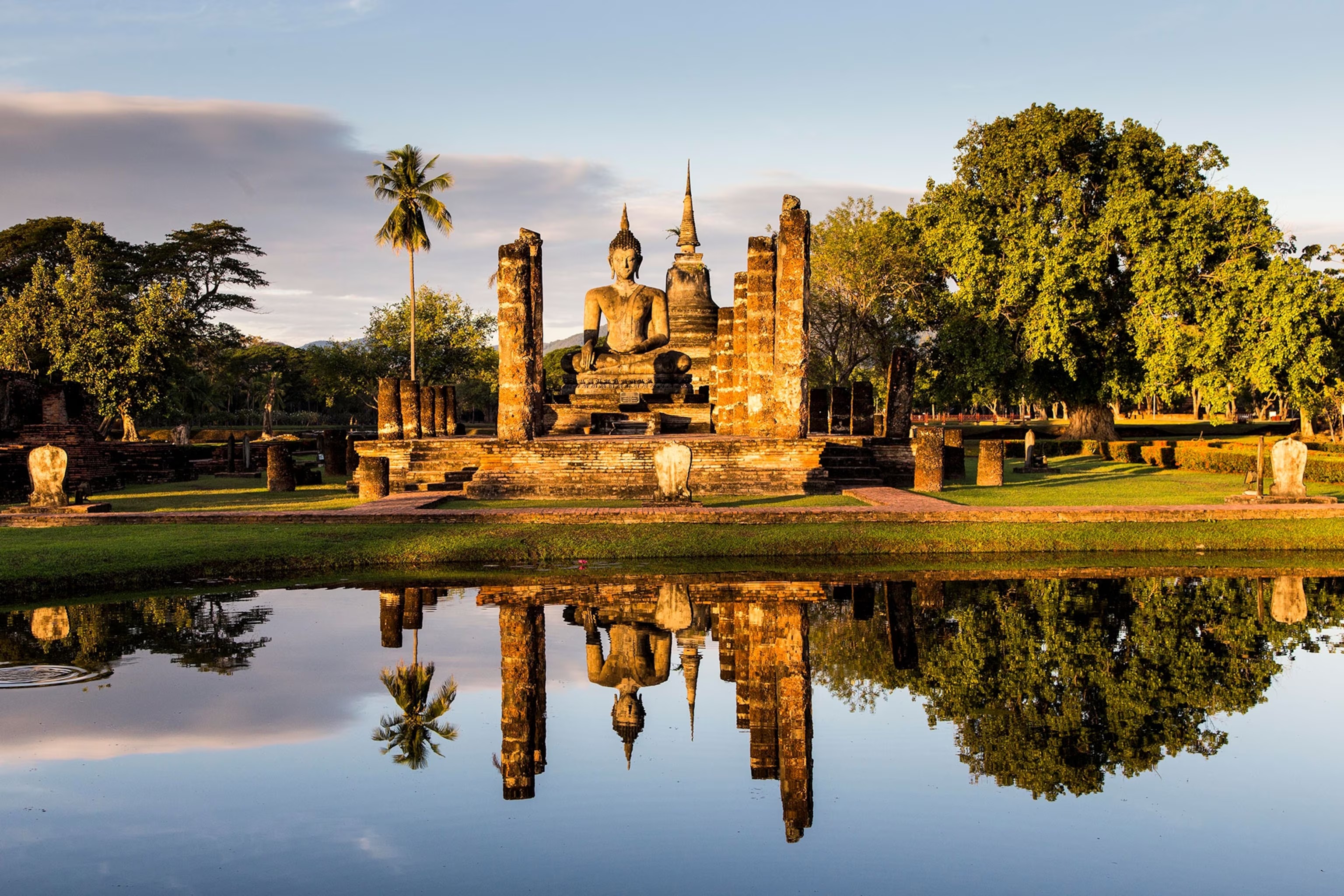 A seated Buddha among the columns of Wat Mahathat, reflected in the pond at Sukhothai