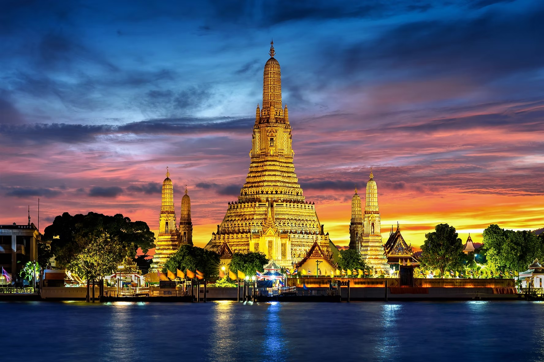 Wat Arun lit at twilight across the Chao Phraya, its prangs against a violet sky